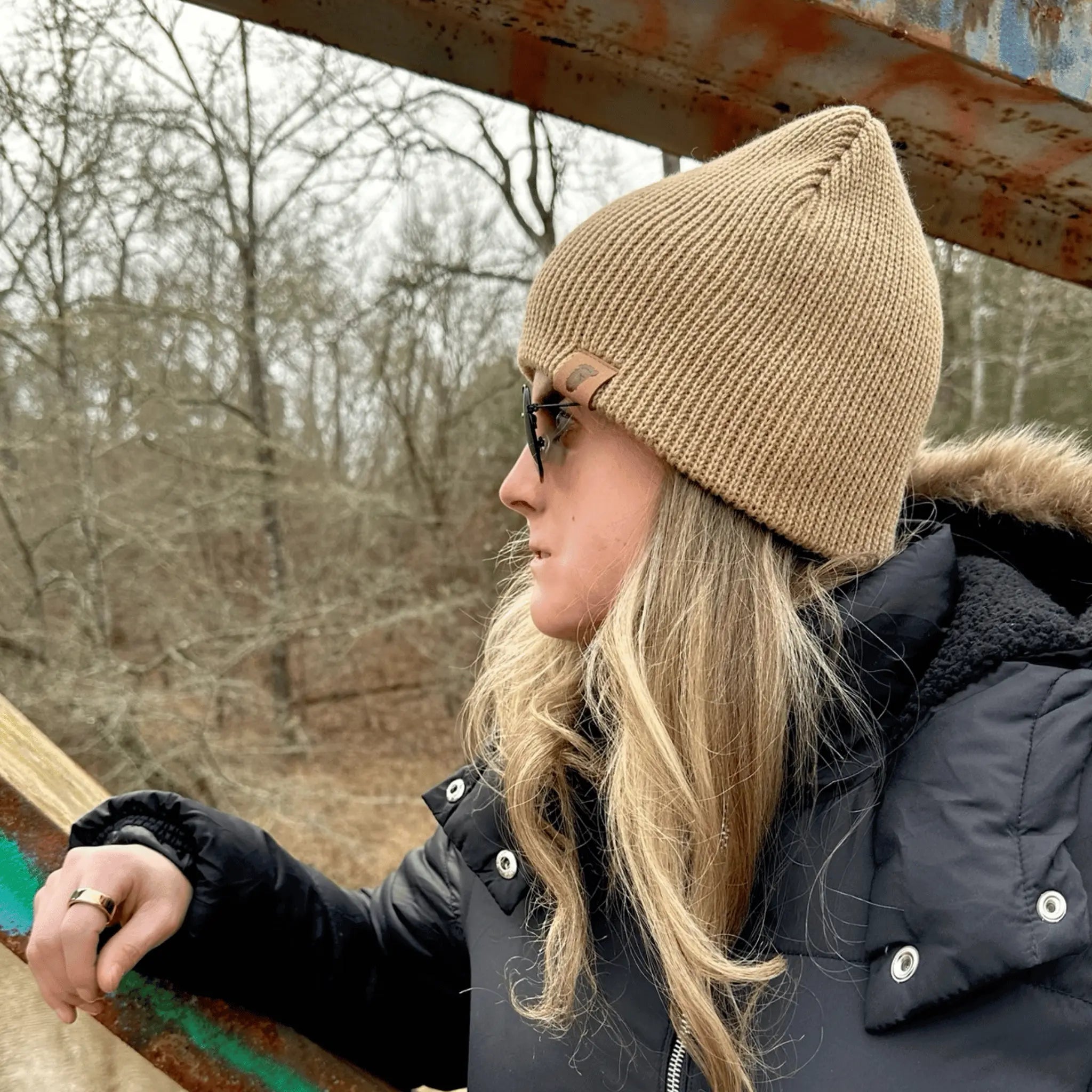 Woman wearing the Skookum Dirt Tan Wilderness Wanderer Beanie — earth-tone knit beanie with leather Bigfoot footprint patch, made for chilly days and Squatch-approved exploring.
