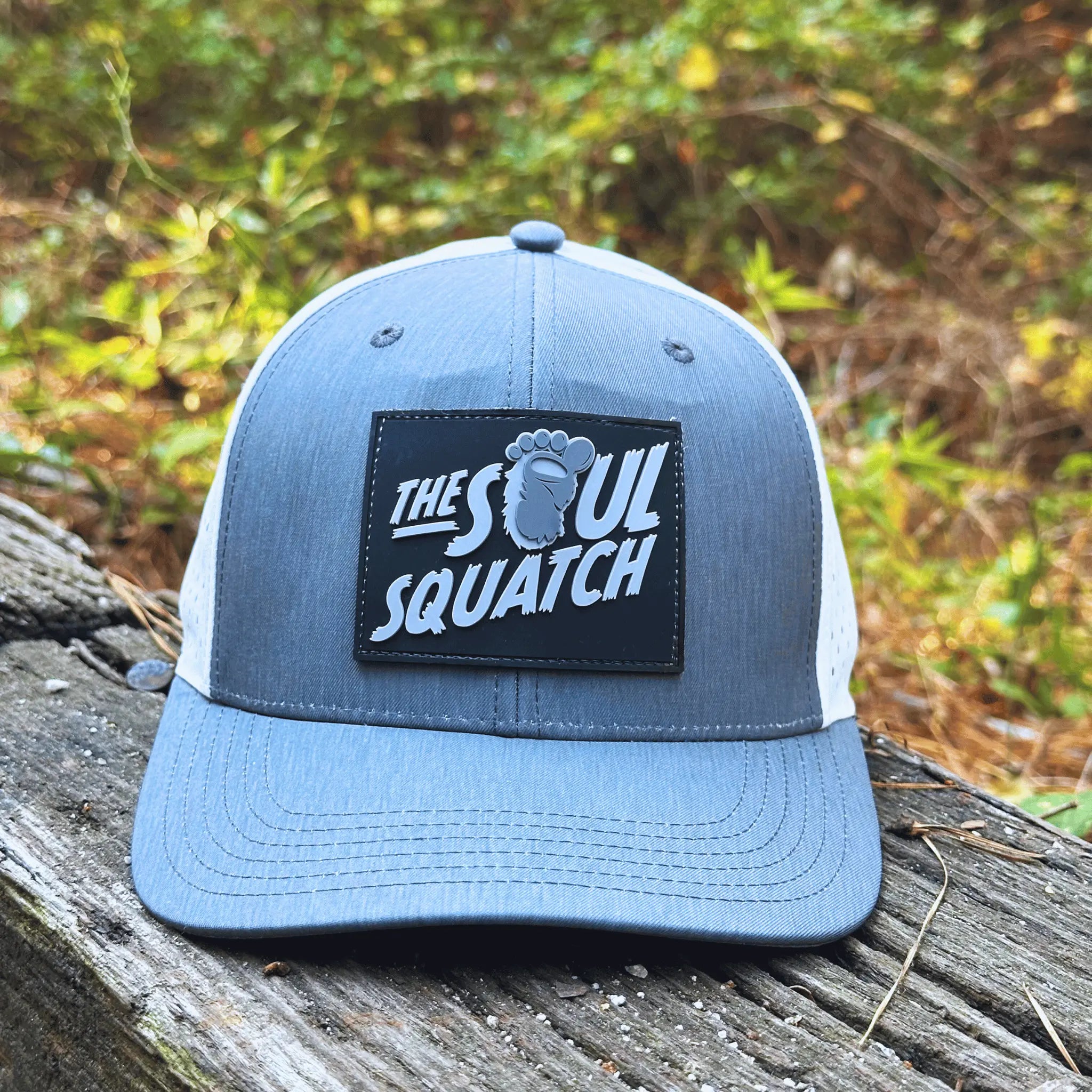 Gray Pathfinder Mid-Profile Hat with white laser-cut ventilation back featured on a woodland log – designed for believers who roam the woods with purpose.