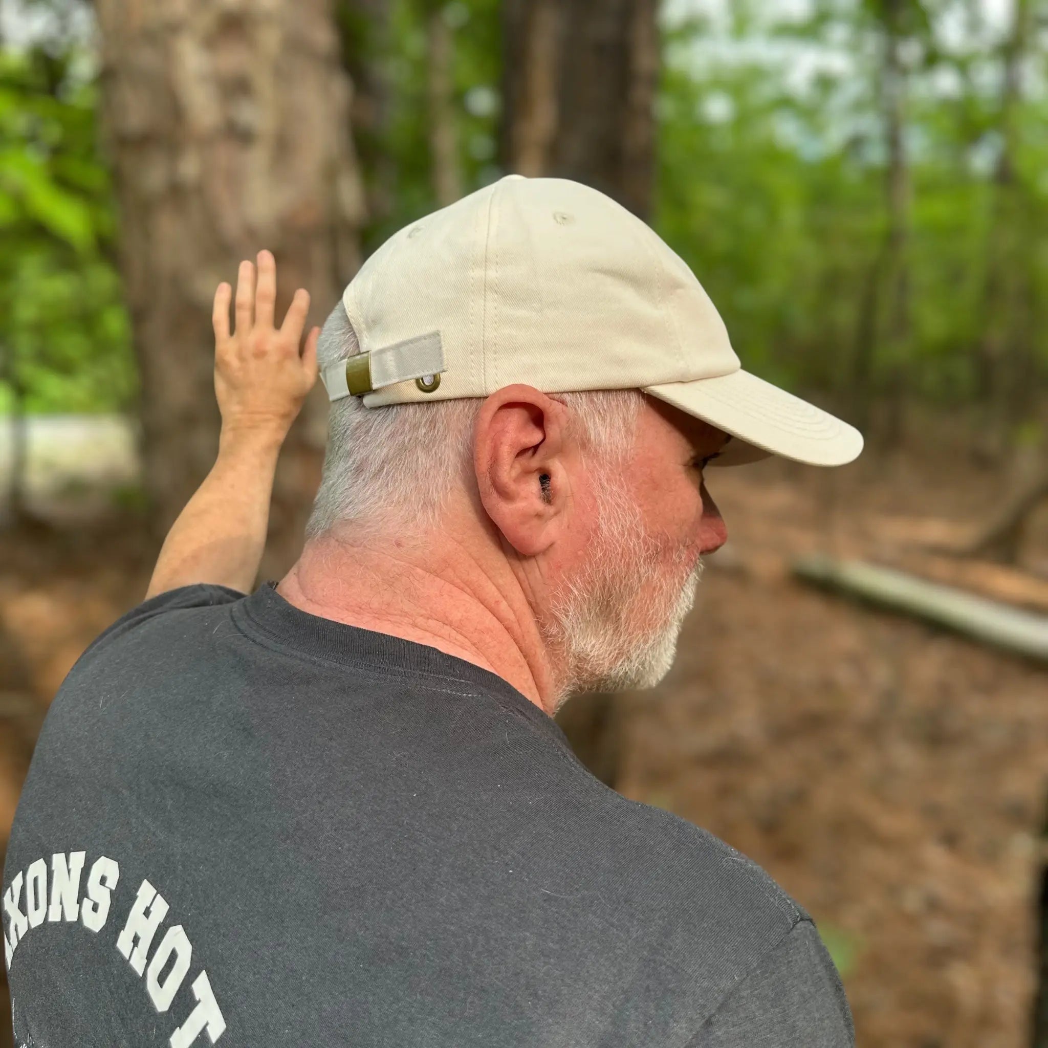 Rear view of a man on a wooded trail wearing the beige Sandstone Trail Dad Hat. The adjustable strap and iconic woven patch highlight its trail-ready, squatch-approved craftsmanship.