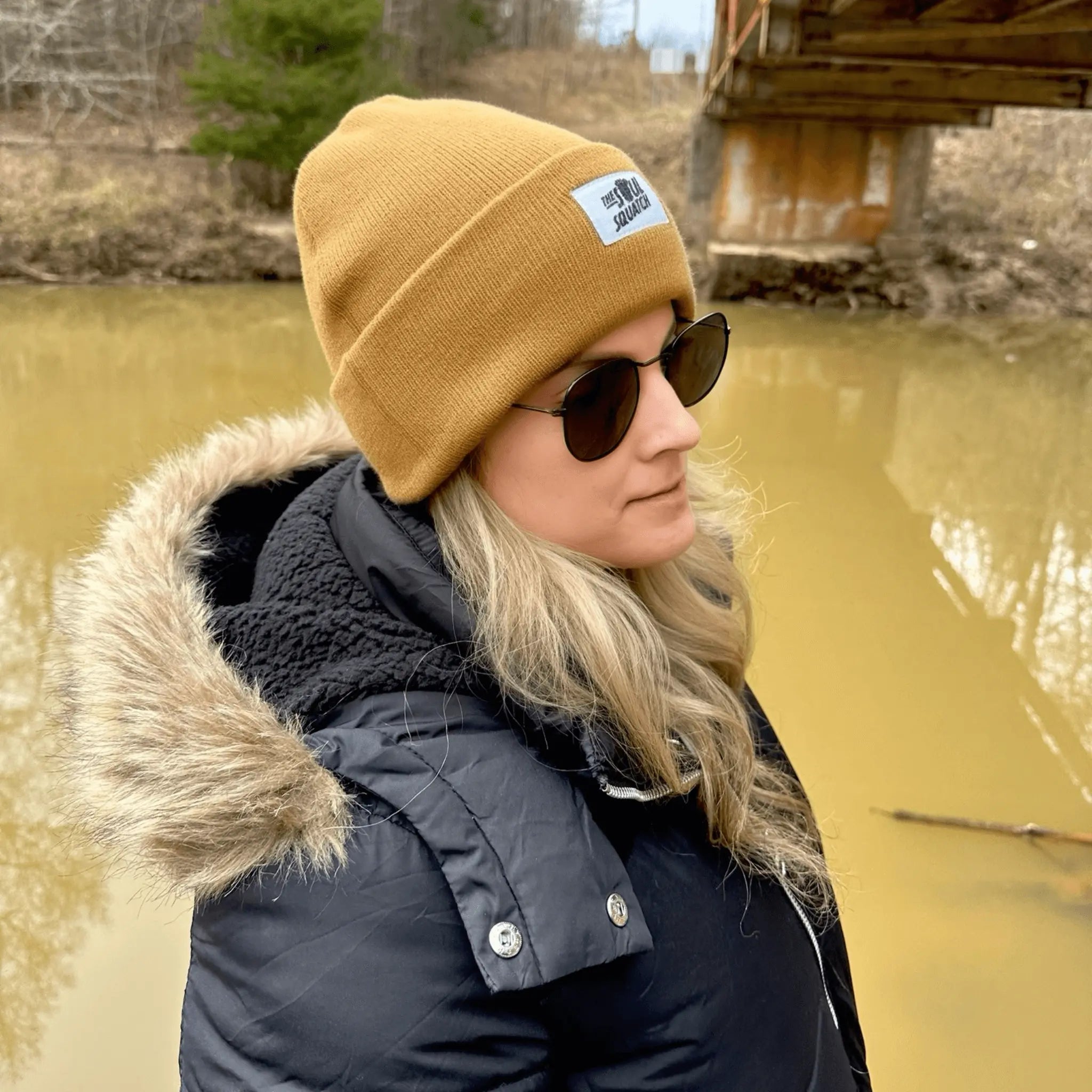 Woman wearing the Woodland Taupe, Sasquatch Soul Beanie — cozy tan knit beanie with The Soul Squatch patch logo, perfect for cool-weather outdoor adventures.