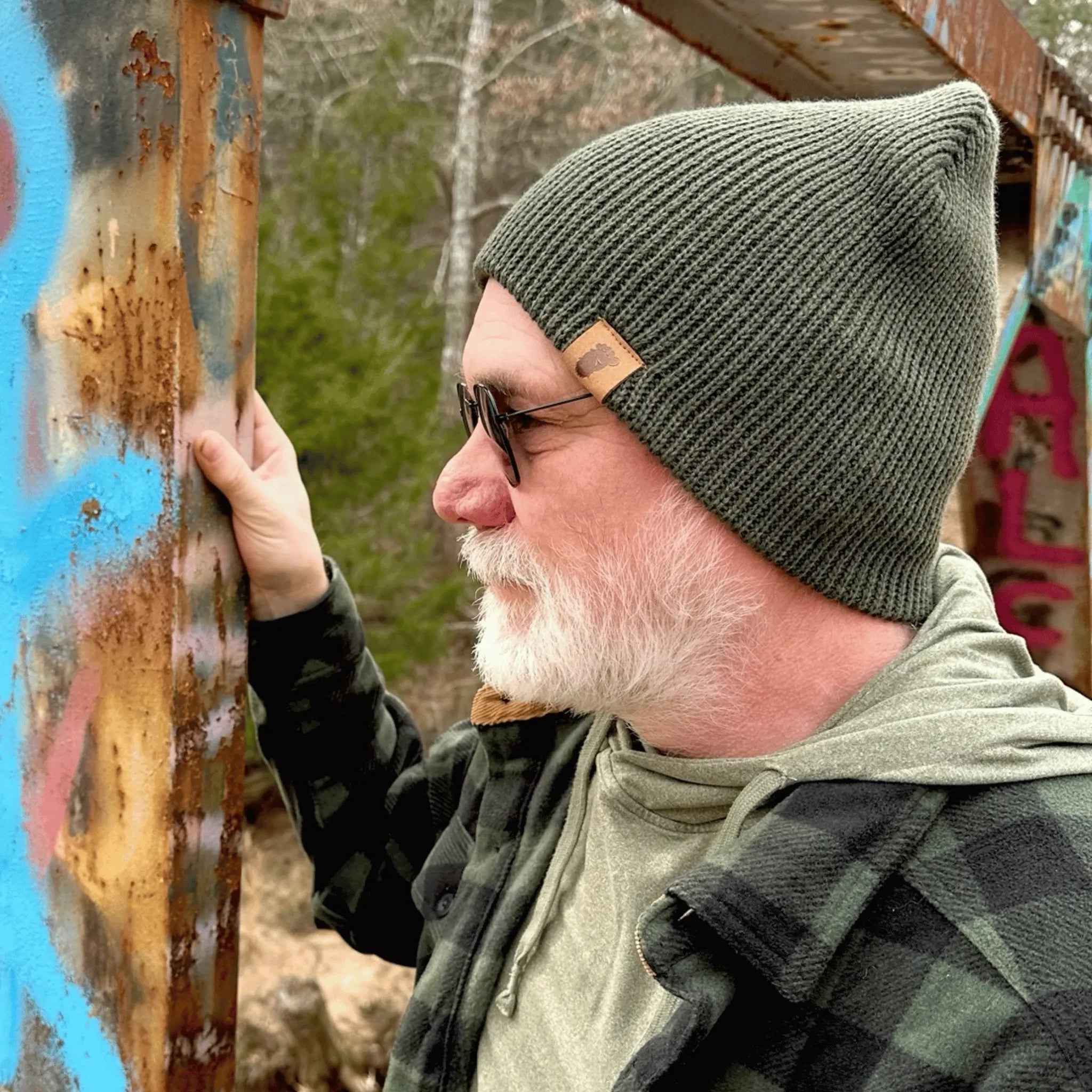Man wearing the Skunk Ape Green, Wilderness Wanderer Beanie — ribbed green outdoor beanie with leather Bigfoot footprint patch, designed for campers and forest explorers.