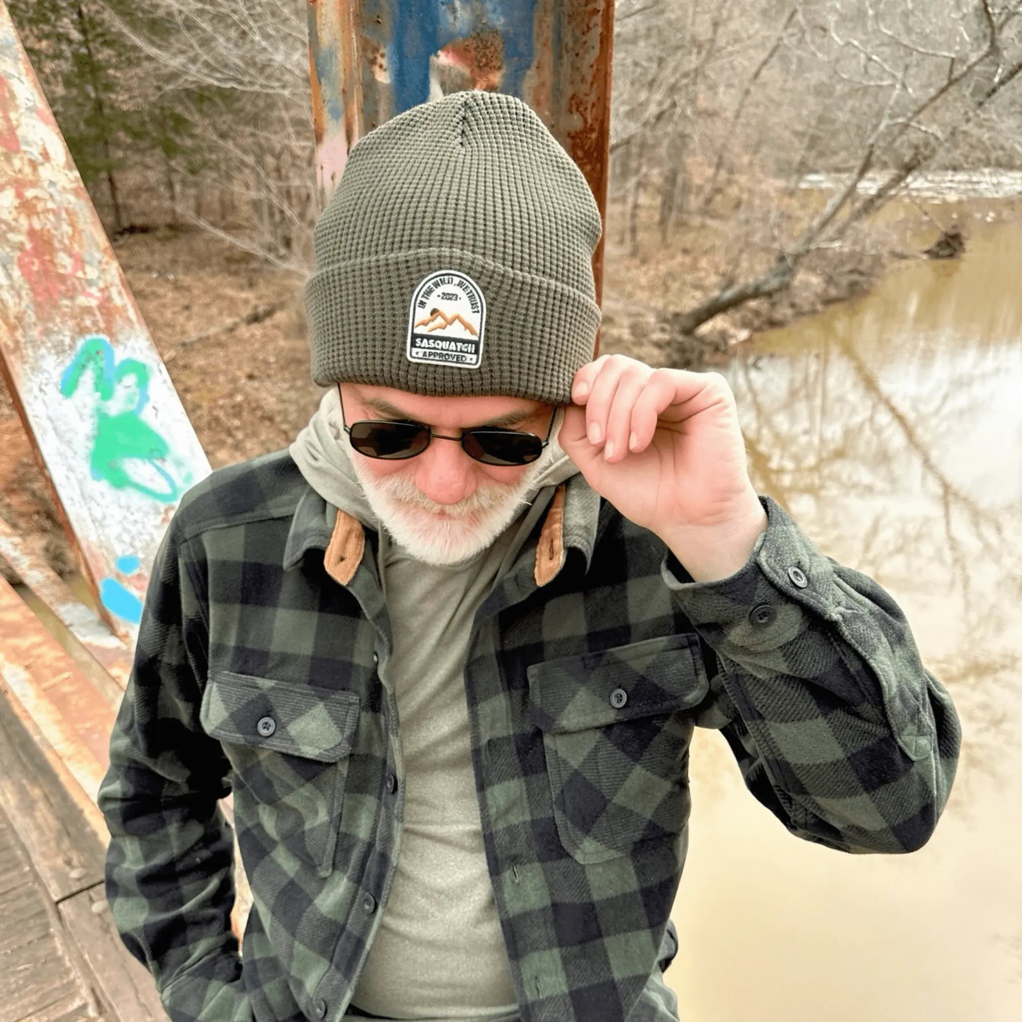 Man wearing the Grassy Knoll Green Sunrise Summit Beanie — rugged green beanie with patch logo, built for trail seekers and campers.