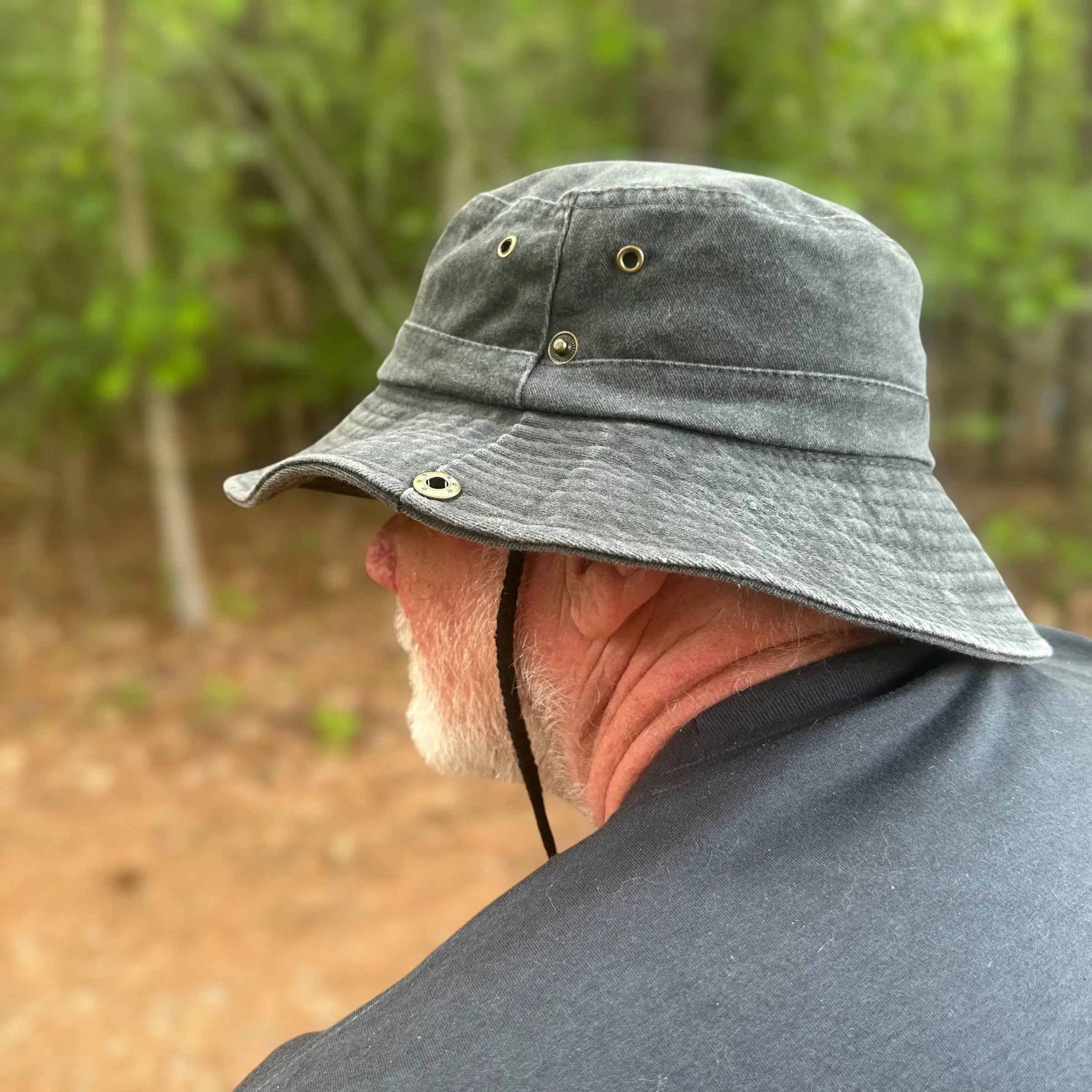 Side profile of a man wearing the black Squatch Scout Boonie Hat in a forest setting, highlighting the adjustable chin strap and breathable structure. A rugged essential for fieldwork and fearless backcountry journeys.