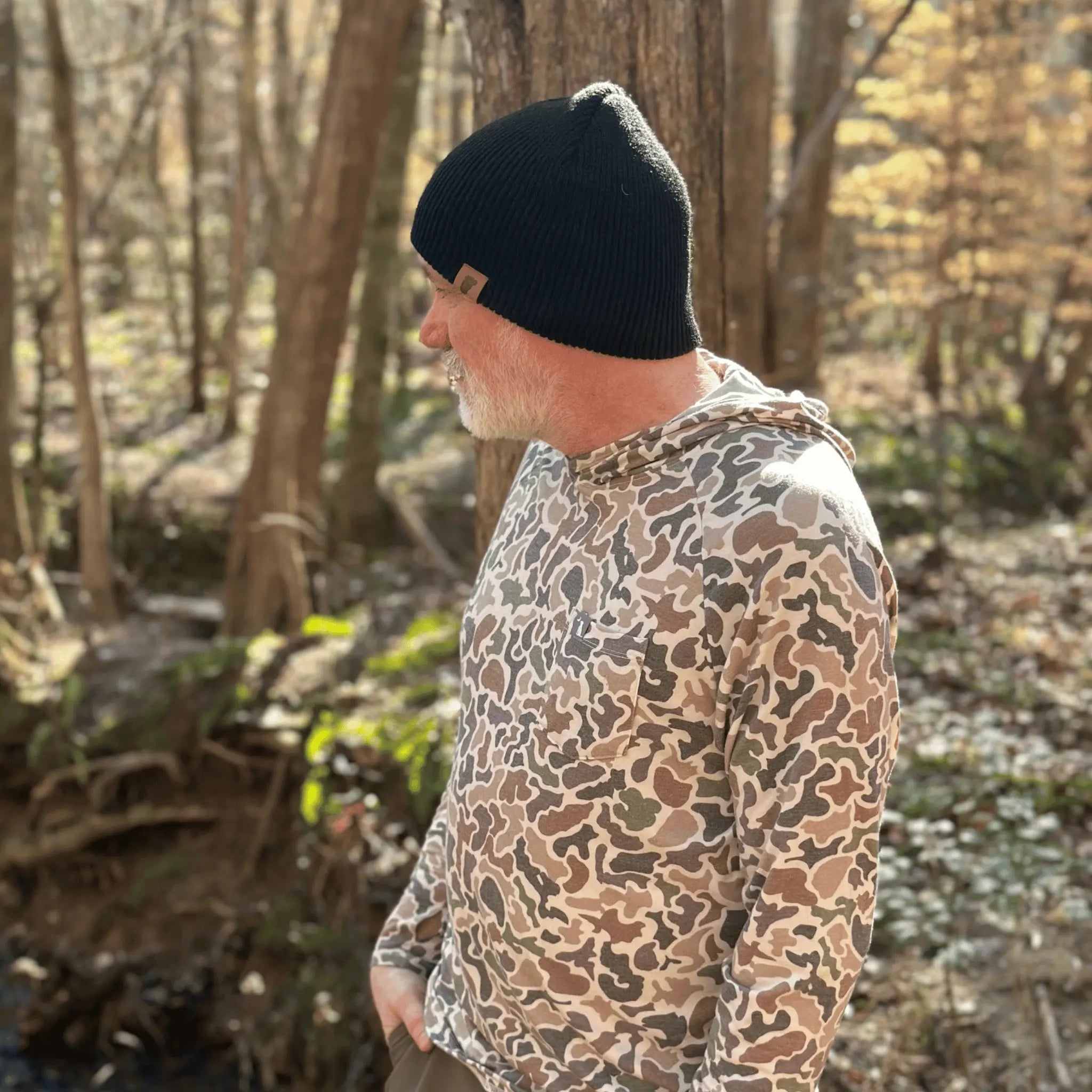 Man wearing the Wood Booger Black Wilderness Wanderer Beanie — rugged black beanie with leather Sasquatch footprint patch, made for trail seekers and cool-weather hikes.