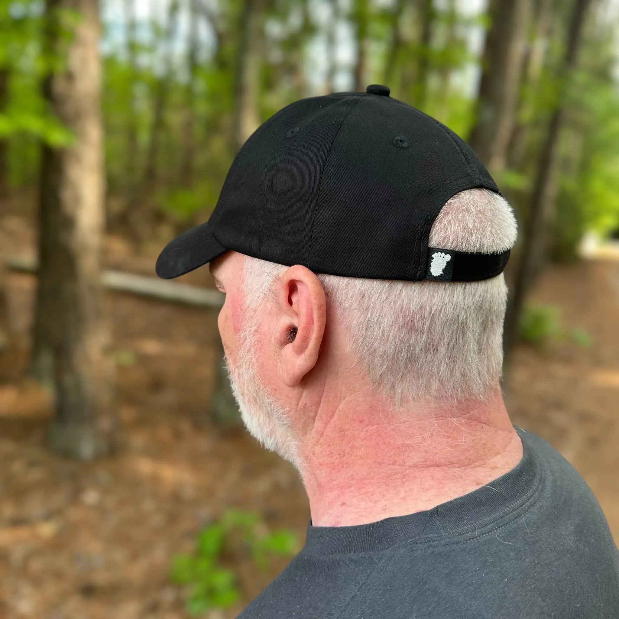 Rear view of the Stealth Pine Dad Hat in the woods, showing off the eco-friendly strap and woven Soul Squatch footprint tag. Built for sustainable style and outdoor comfort.
