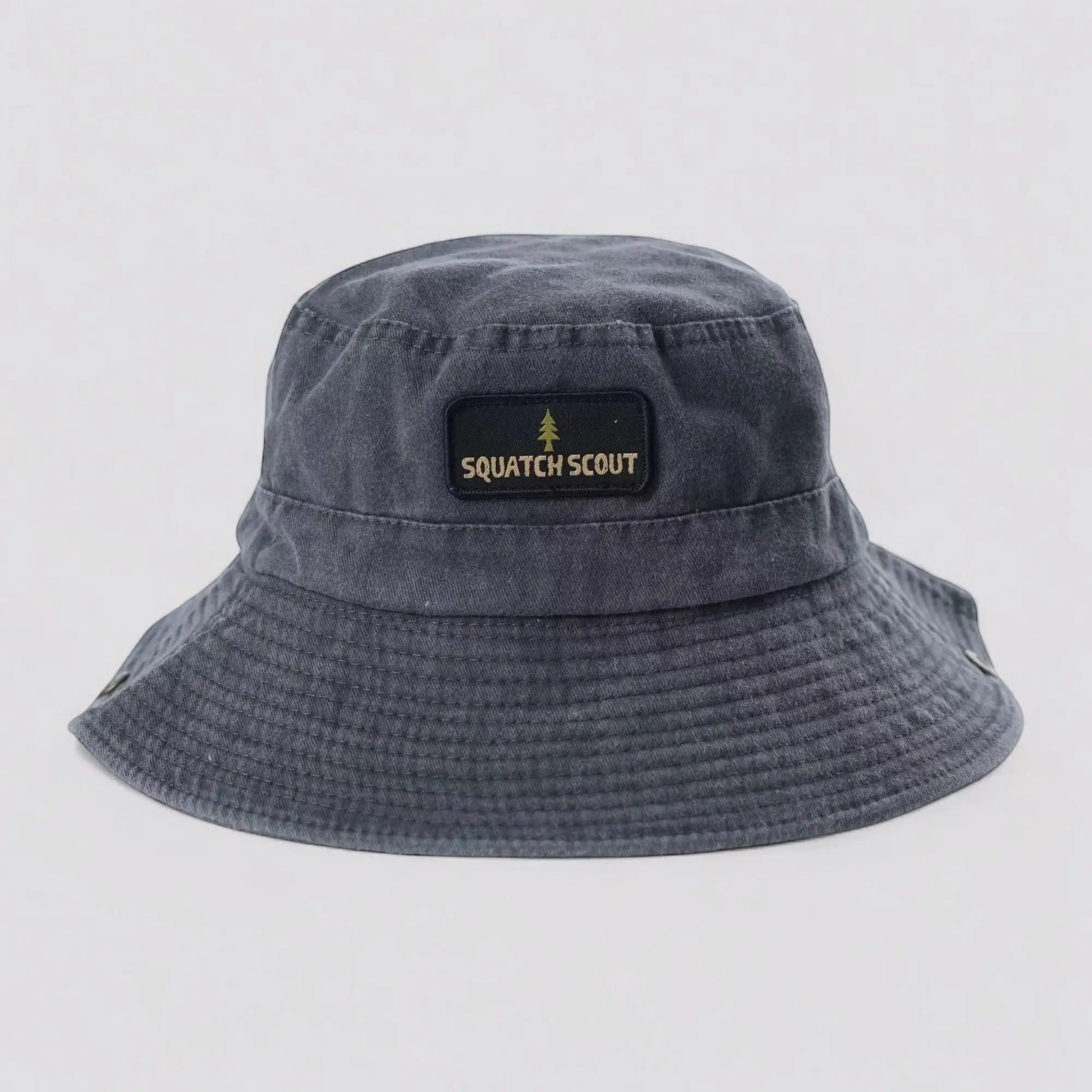 Flat lay of the Squatch Scout Boonie Hat in vintage black, featuring a centered Squatch Scout woven patch with pine tree emblem. A wide-brimmed cotton boonie hat designed for off-grid explorers, hikers, and Bigfoot believers.