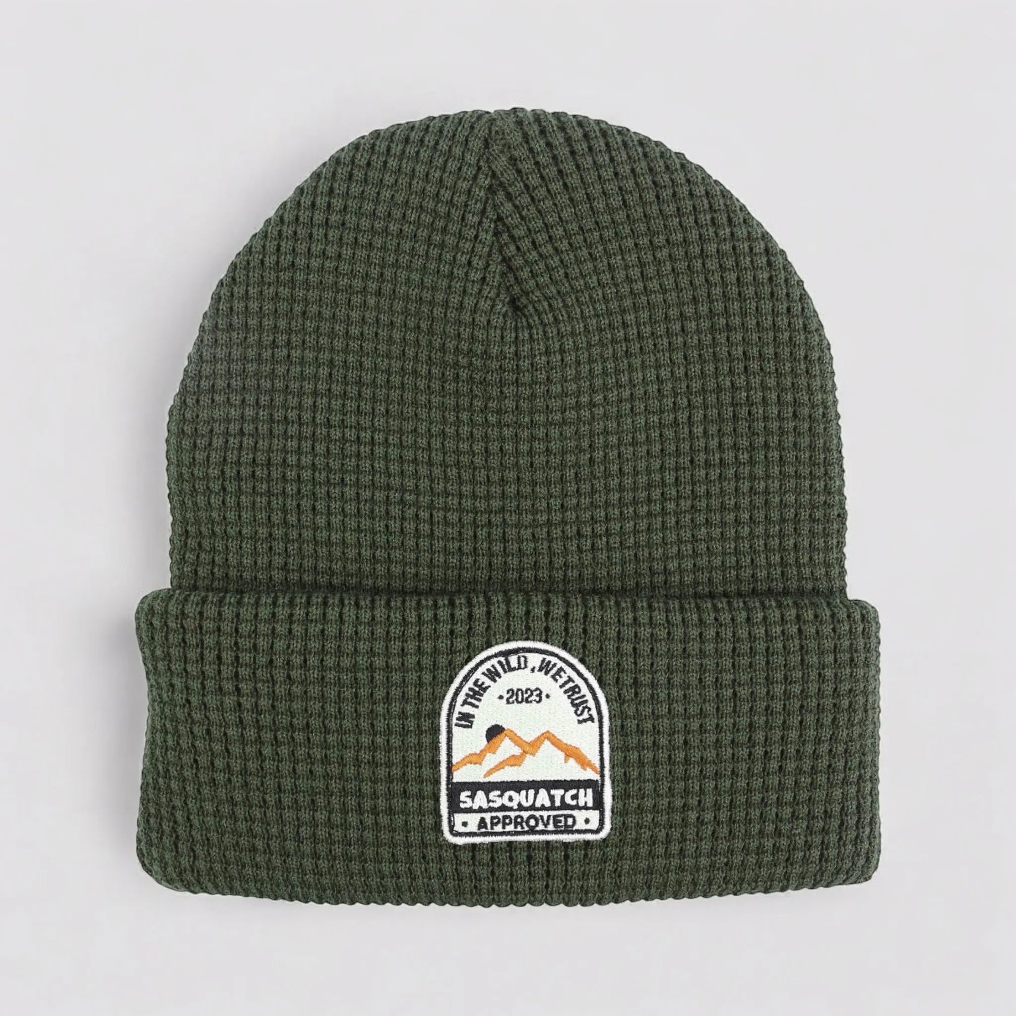 Flat lay of the Sunrise Summit Beanie in Grassy Knoll Green — earth-tone green waffle-knit beanie with mountain trail patch.