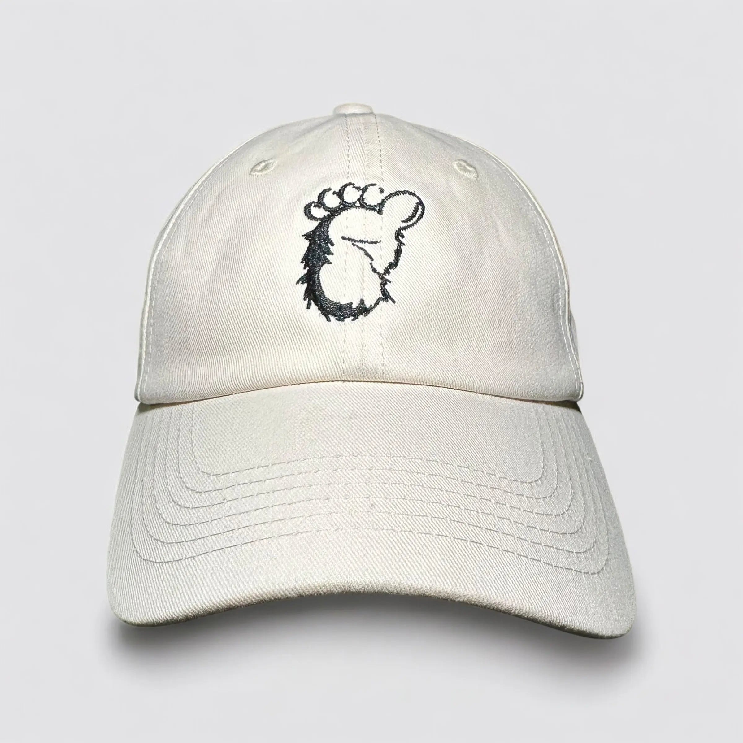 Flat lay of the Sandstone Trail Dad Hat in beige, featuring a bold black embroidered Sasquatch footprint on the front. Made from 100% recycled cotton, this eco-conscious cap is perfect for hikers, wanderers, and nature lovers.